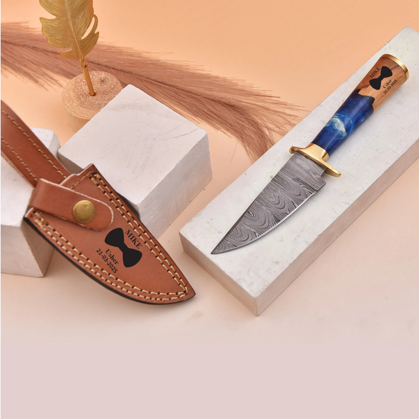 Decorative knife with blue blade and brown sheath on a white stand against a beige background for wedding usher gifts
